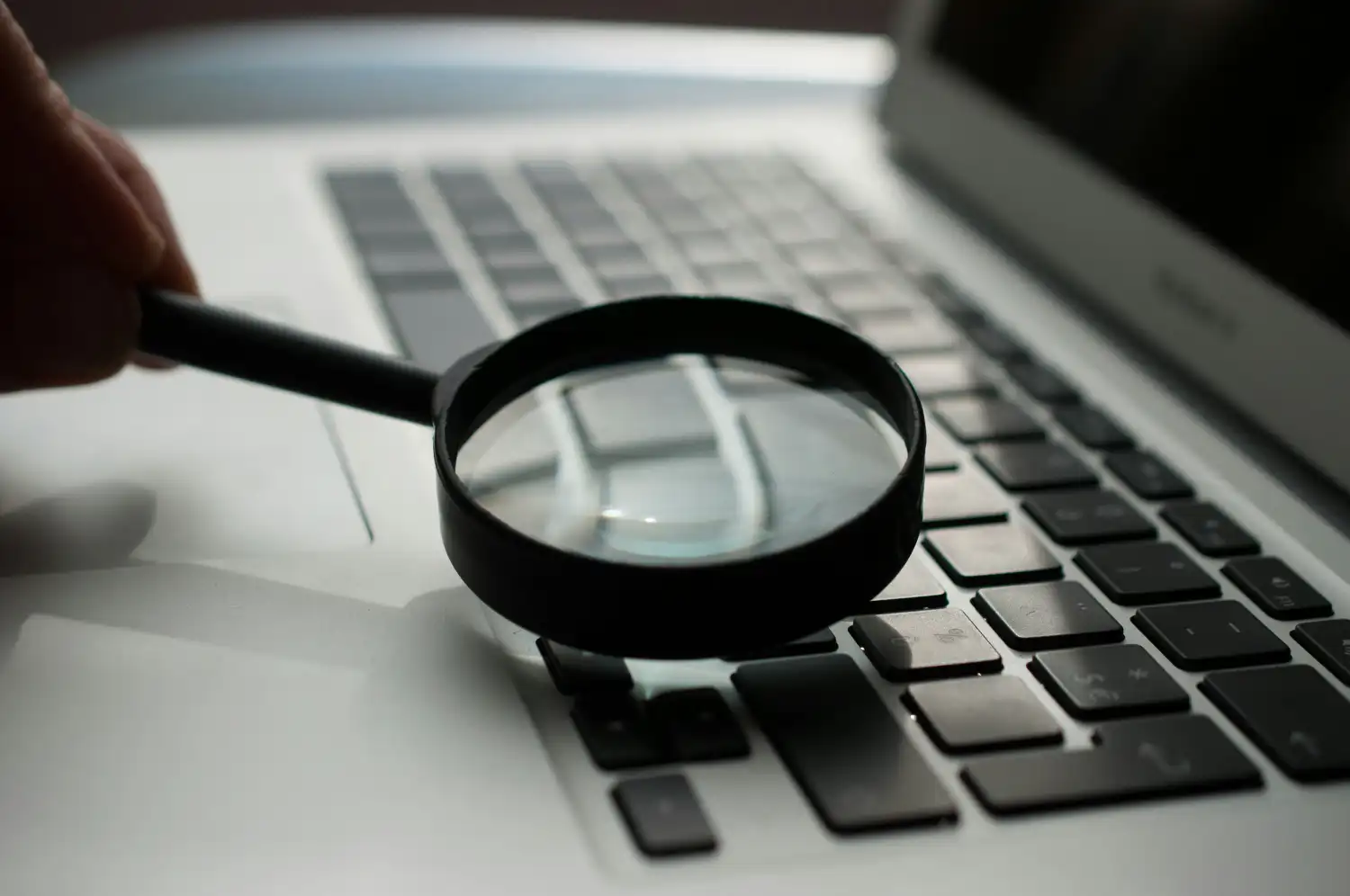 Close-up of a designer using a magnifying glass on a laptop keyboard, symbolizing meticulous attention to detail and high-quality web development standards.