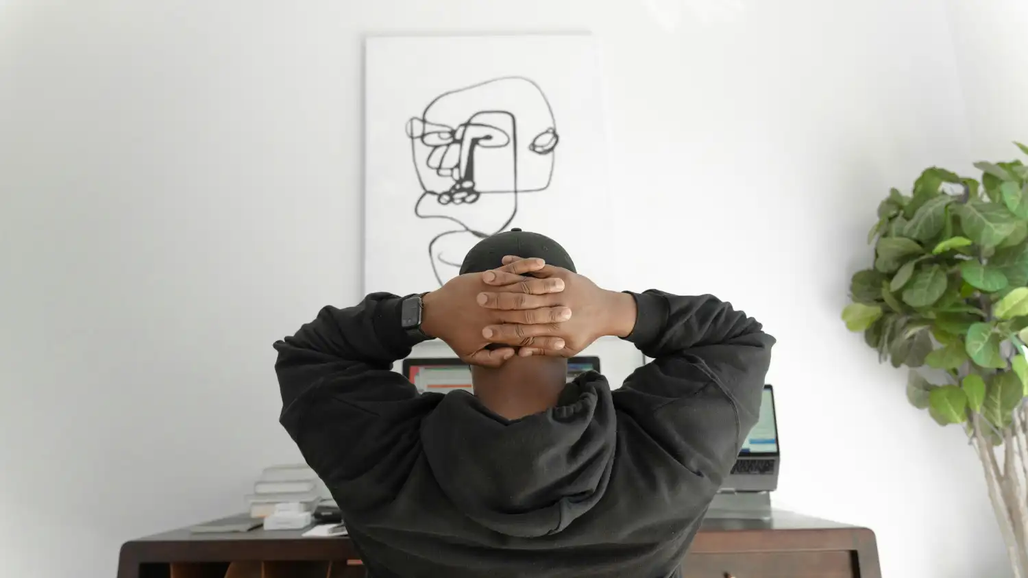 Back view of a creative director leaning back at a minimalist desk with abstract line art on the wall, symbolizing design judgment and taste over automated AI execution.
